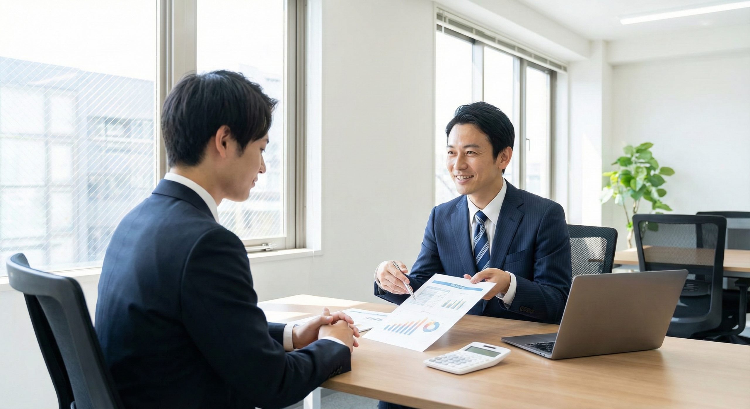 明るい日差しが入る葬儀社のオフィスで、新人スタッフに給与体系の説明をしている採用担当者の様子