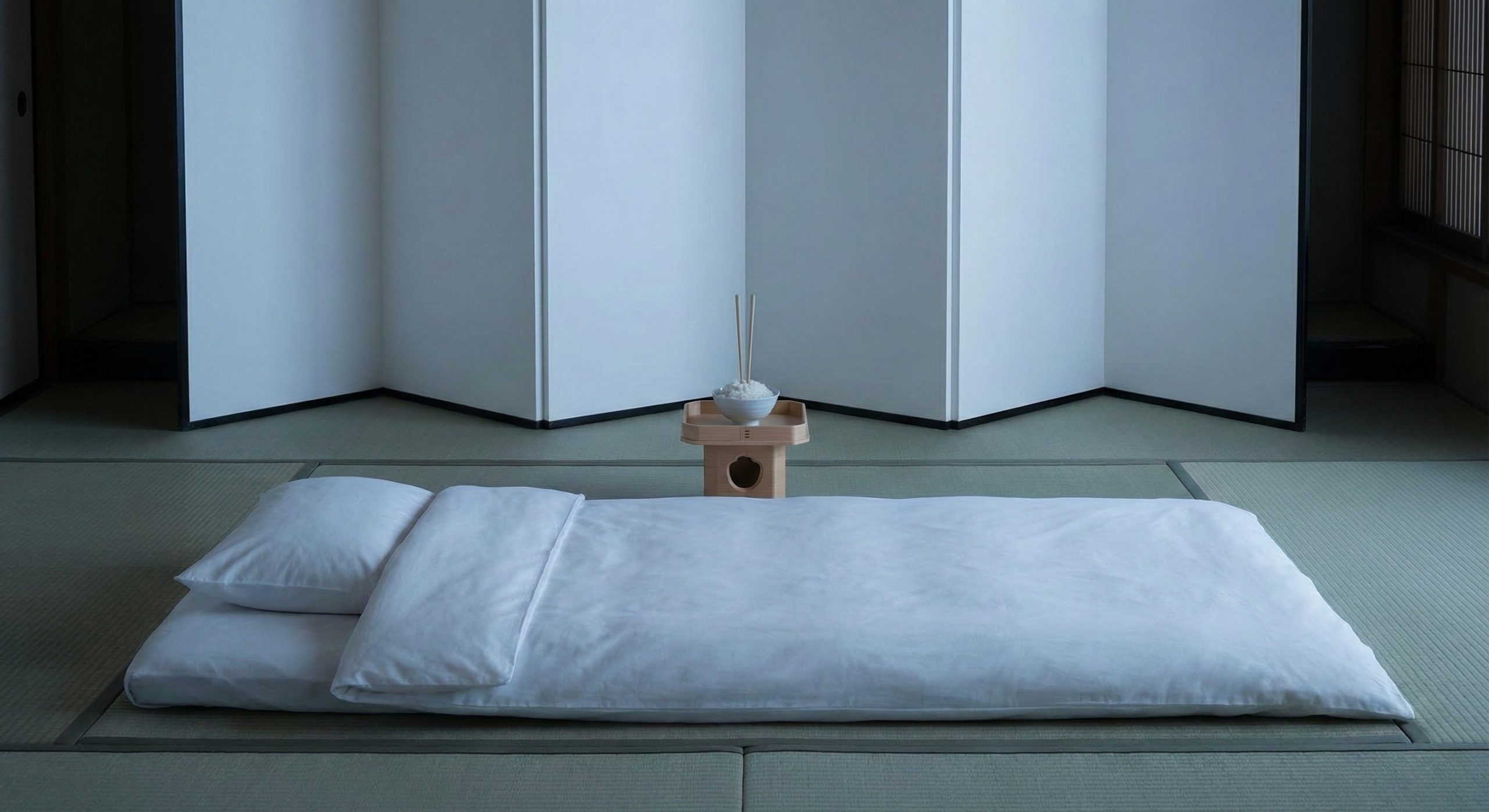 厳粛な和室で、葬儀の儀式として逆さ屏風が立てられ、北枕で安置された布団の枕元には一本の線香と枕飯が供えられている様子。