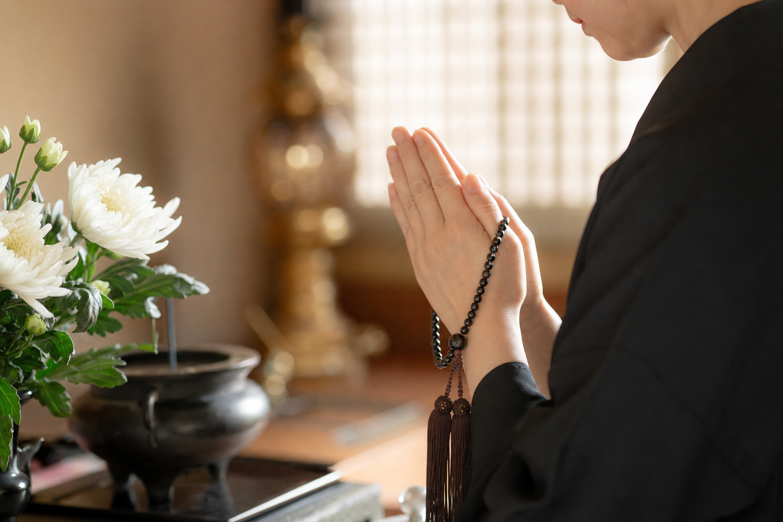静かに合掌する手元と数珠、白い菊の花