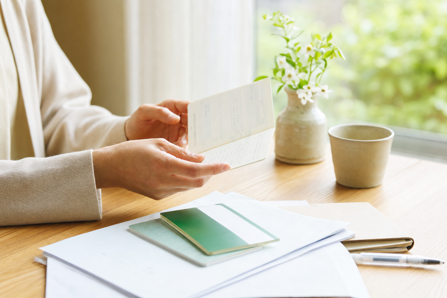 通帳と書類を整理する手元、窓辺の柔らかい光