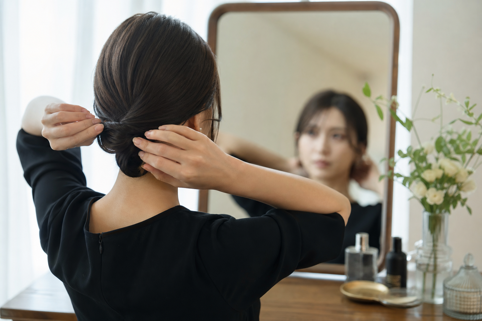 鏡の前で髪を低い位置でまとめる女性の手元